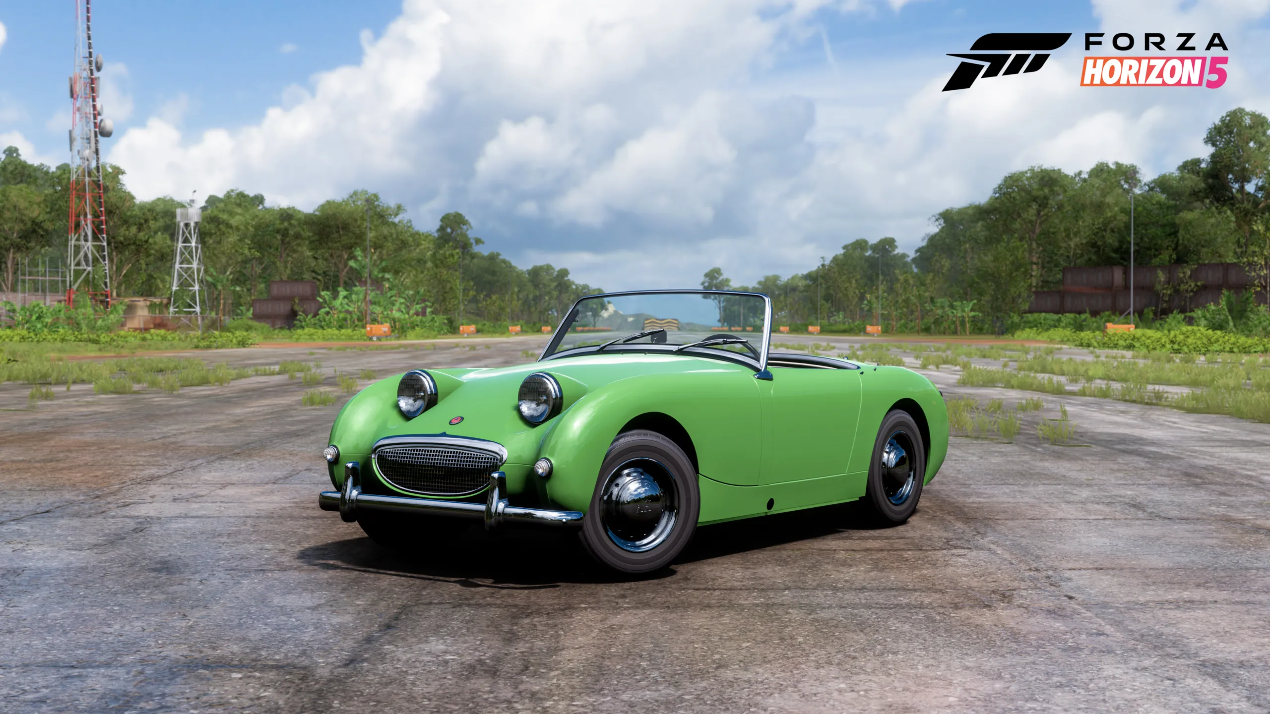 A green Austin Healey Sprite sitting on a tarmac road with trees either side of it.